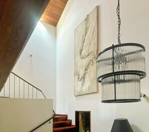 A staircase with a wooden handrail, a hanging chandelier, and a marble wall art piece. - Galician stone house with hórreo and garden (Bustelo)