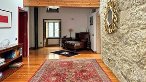 A spacious living room with a high ceiling, wooden beams, a fireplace, a large rug, and a stone accent wall. - Galician stone house with hórreo and garden (Bustelo)