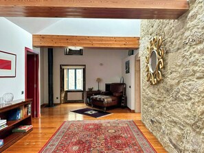 Ein geräumiges Wohnzimmer mit hohen Decken, Holzbalken, einem Kamin, einem großen Teppich und einer Wand mit Steinverkleidung.