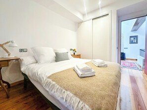 Un dormitorio con cama, mesita de noche, lámpara y vistas al exterior.