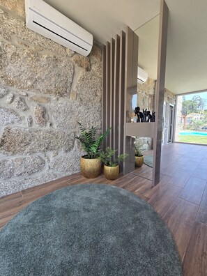 A modern interior with a stone wall, a large air conditioning unit, and a view of a pool through a glass door. - Vale do Luar House (Celorico de Basto)