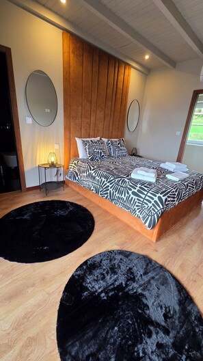 Ein modernes Schlafzimmer mit einem großen Bett, zwei runden schwarzen Teppichen, einem hölzernen Kopfteil und einem kleinen Nachttisch mit Lampe.