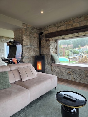 A cozy living room with a stone wall, a fireplace, a sofa, and a view of a green landscape. - Vale do Luar House (Celorico de Basto)