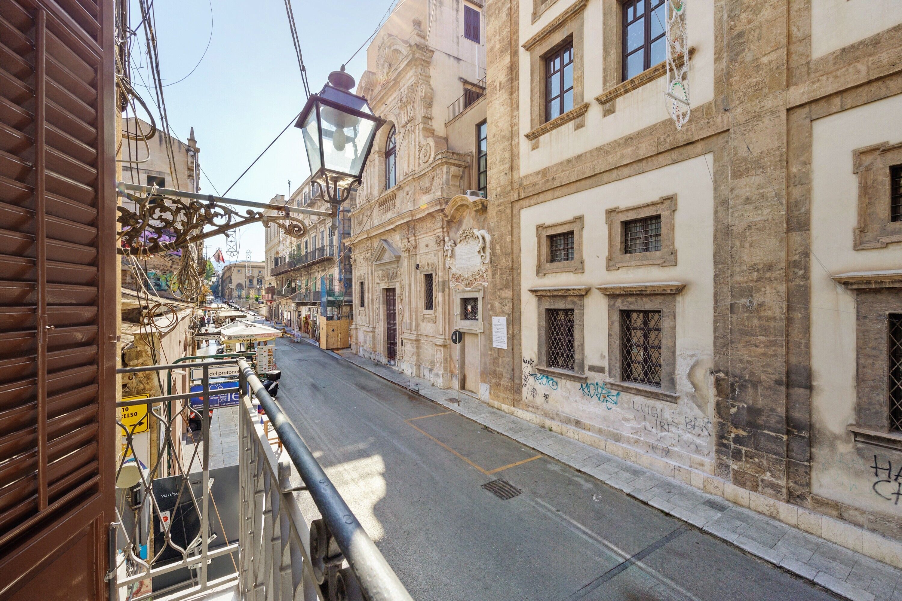 A narrow street with buildings on either side, featuring balconies and a street lamp.