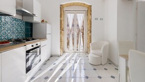 Una cocina moderna con estufa, horno y armarios blancos. Se ve un ventanal con cortinas y vistas al exterior.