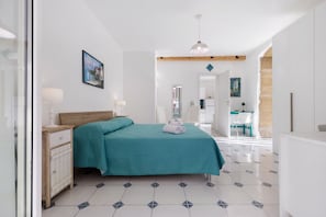 Ein Schlafzimmer mit einem Bett, Nachttischen, einem Wandbild, einer Pendelleuchte und einem durch eine offene Tür einsehbaren Badezimmer.