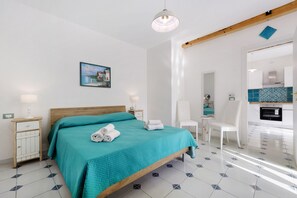 Une chambre à coucher moderne avec un lit, des tables de chevet, un tableau et une vue sur la cuisine.