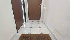 Un pasillo con felpudo, una puerta y piso de baldosas.