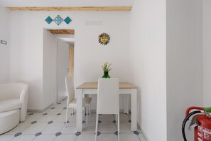 A room with a white sofa, a wooden dining table with two chairs, and a small green vase with flowers. - Apartment 'Le Stanze Del Sole - Verde' with Balcony and Air Conditioning (Palermo)