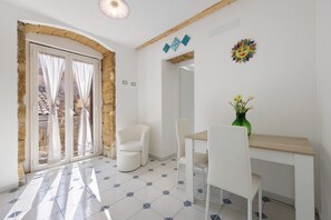 Un comedor con mesa y sillas, un florero con flores y vistas a través de un ventanal.