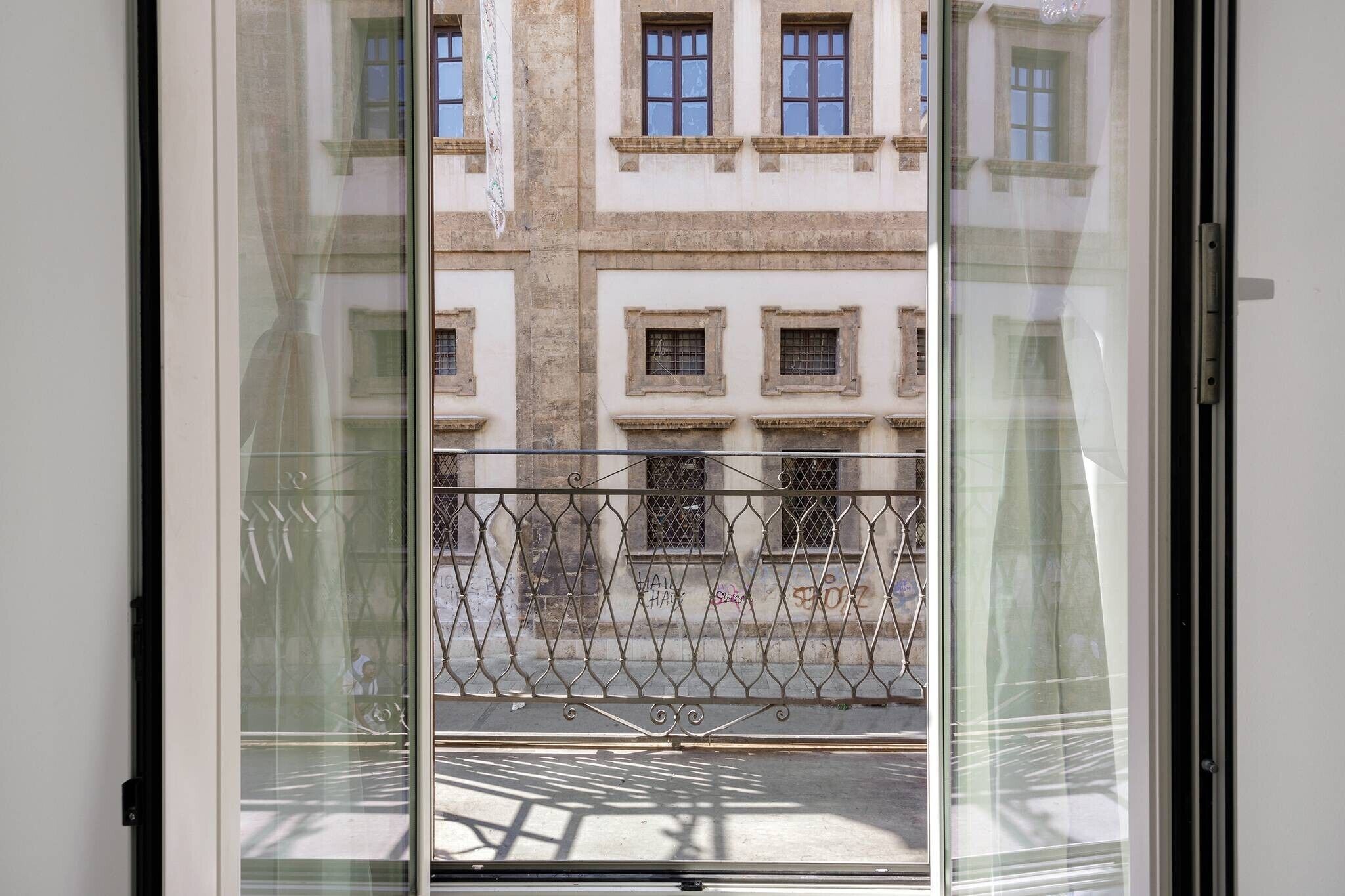 A view through a window with a metal fence, a street, and buildings with multiple windows.