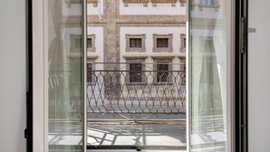 Blick durch ein Fenster mit Metallgitter, einer Straße und Gebäuden mit zahlreichen Fenstern.