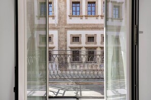 Blick durch ein Fenster mit Metallgitter, einer Straße und Gebäuden mit zahlreichen Fenstern.