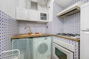 Ett kompakt kök med en gasspis, en tvättmaskin och en diskho med en bänkskiva i trä.
