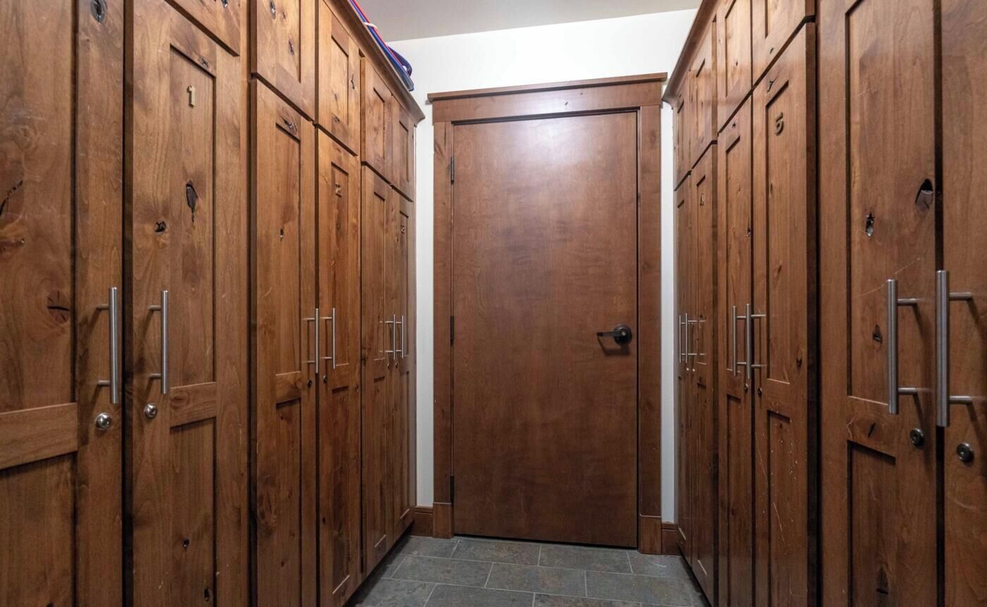 A hallway with wooden lockers, a tiled floor, and a closed door at the end.