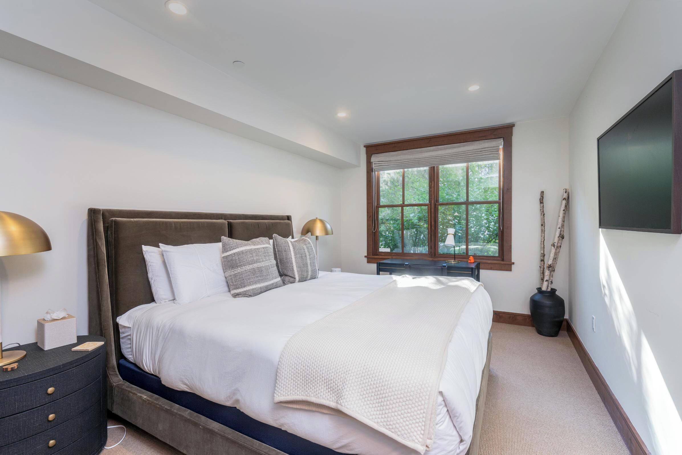 A bedroom with a large bed, bedside tables, a window with a view, and a wall-mounted TV.