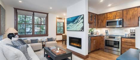A modern living room with a fireplace, a dining area, and a kitchen with wooden cabinets and stainless steel appliances.