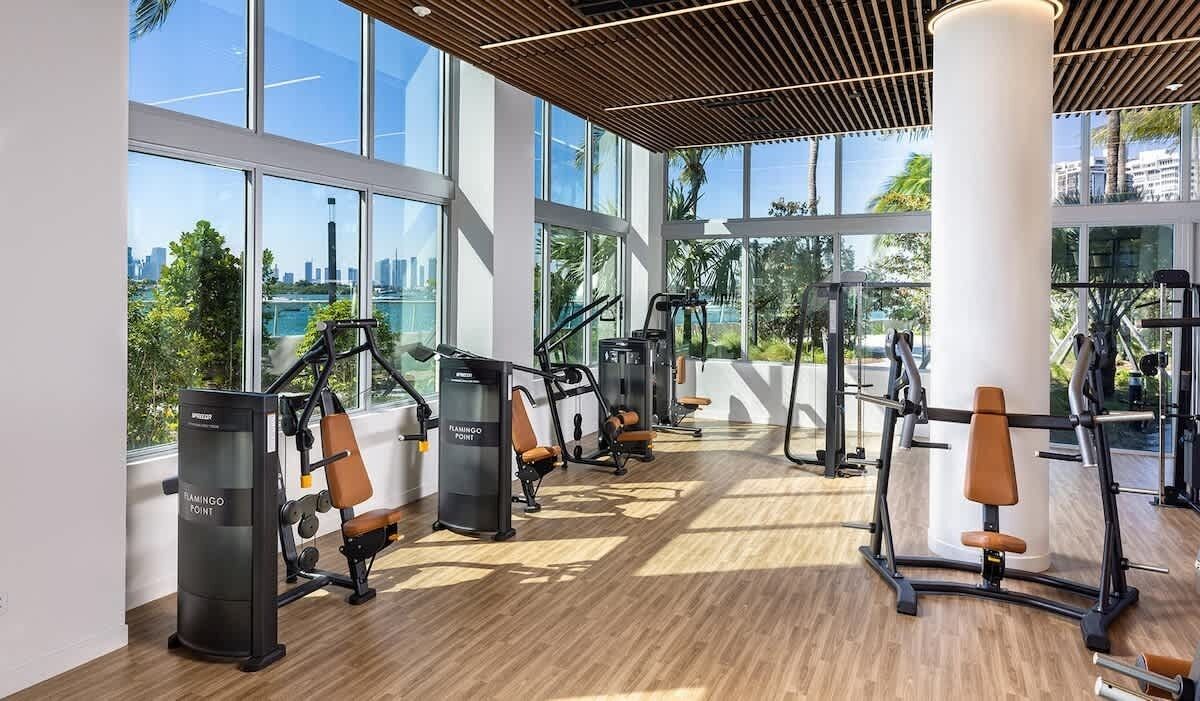 A gym with cardio machines, weight benches, and a large window offering a city view.