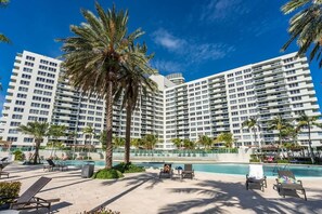 A large hotel with multiple floors, a swimming pool, and palm trees. - Monthly 2BR Penthouse · City + Ocean Views, SoBe (Miami Beach)