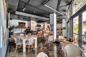 L’intérieur d’un restaurant est aménagé avec des meubles en osier, un coin bar et une grande fenêtre.