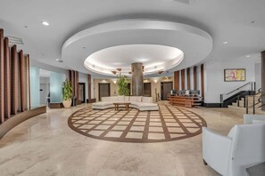 Eine geräumige Lobby mit einer zentralen Sitzecke, einer Treppe und einer Rezeption.