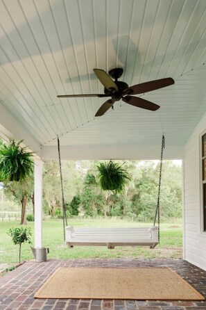 A porch with a ceiling fan, a swing, and a view of a grassy area.