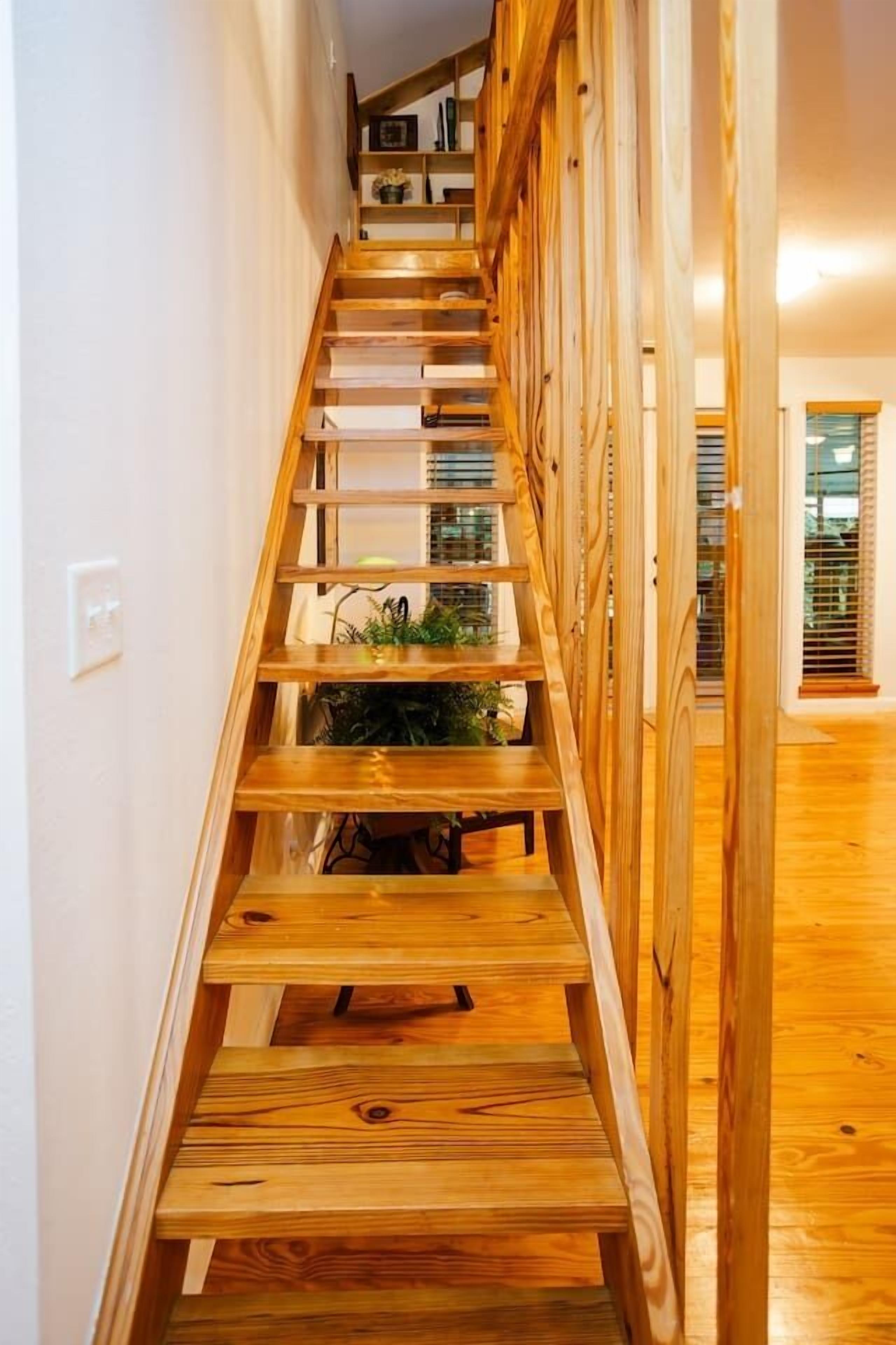 A wooden staircase with a railing, leading to a landing area with a plant.