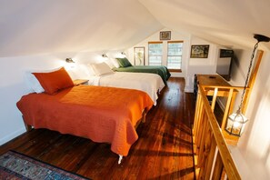 A bedroom with two beds, wooden flooring, and a small table with a lamp.