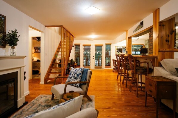 A spacious living room with a wooden staircase, a dining area with wooden chairs, and a fireplace.