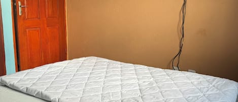 A bedroom with a bed, a wooden door, and a wall-mounted TV.