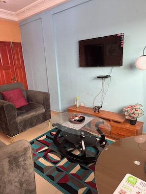 A living room with a sofa, a glass coffee table, a TV mounted on the wall, and a wooden sideboard.