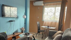 Ein Wohnzimmer mit einer Couch, einem Couchtisch, einem Fernseher und einem Essbereich mit einem Stuhl und Tisch.