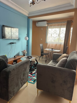 A living room with a sofa, a coffee table, a TV, and a dining area with a chair and table.