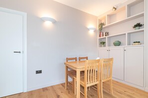 A dining area with a wooden table and chairs, a white door, and a shelving unit with plants and decorative items. - Beautifully Refurbished 2Bed Flat in East Finchley - Pass the Keys (London)