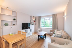 A modern living room with a flat-screen TV, wooden furniture, and a large window with curtains. - Beautifully Refurbished 2Bed Flat in East Finchley - Pass the Keys (London)