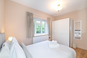 A hotel room with a bed, a window with curtains, a radiator, a wardrobe, and a mirror on the wall. - Beautifully Refurbished 2Bed Flat in East Finchley - Pass the Keys (London)