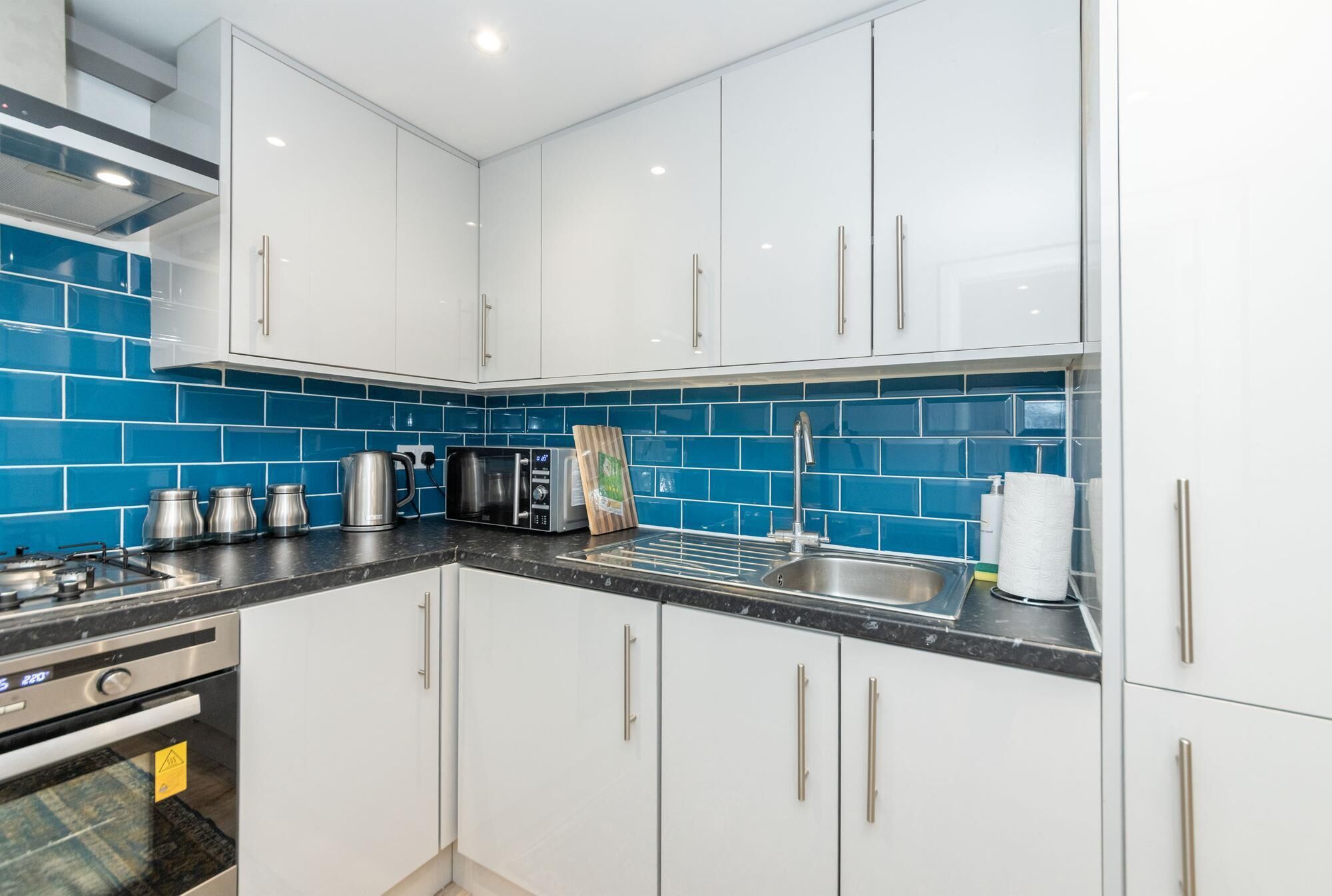 Een moderne keuken met witte kasten, een zwart aanrecht en blauwe spatborden.