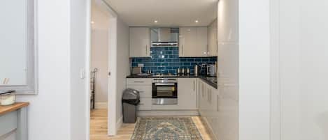 A compact kitchen with white cabinets, a blue backsplash, and a patterned rug on the floor.