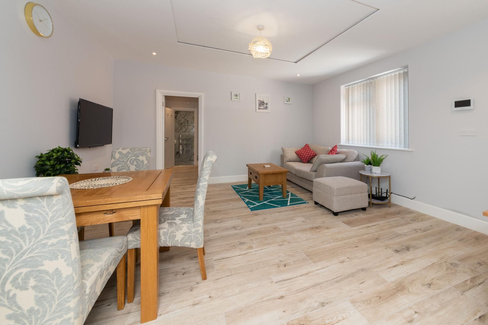 Un salon moderne avec une table à manger en bois, deux canapés, une table basse et un téléviseur fixé au mur.