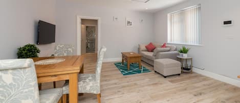 A modern living room with a wooden dining table, two sofas, a coffee table, and a TV mounted on the wall.