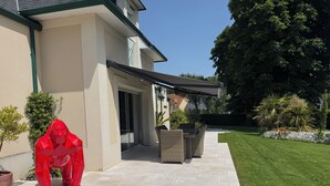 Eine Terrasse mit überdachter Sitzgelegenheit, einer Schiebetür und einem gepflegten Rasen.
