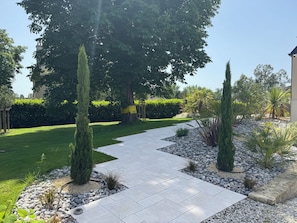 A landscaped garden with a paved walkway, neatly trimmed hedges, and a variety of shrubs and trees.