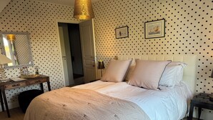 Ein ordentlich eingerichtetes Schlafzimmer mit einem Bett, Nachttischen, einer Kommode, einem Spiegel und einer Tür zu einem anderen Raum.