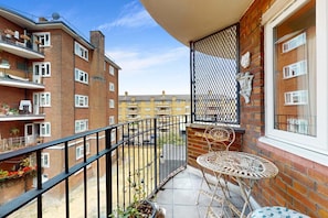 A balcony with a metal railing, a small table, and chairs, surrounded by brick buildings. - Artful Hoxton Flat with Private Balcony - Pass the Keys (London)