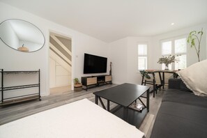 A modern living room with a flat-screen TV, a sofa, a dining table, and a staircase.