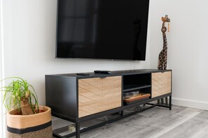 A modern living room with a flat-screen TV mounted on the wall, a wooden and black console table with drawers, a giraffe decoration, and a potted plant.