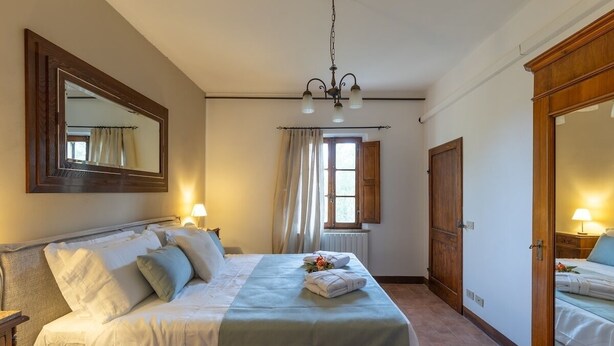Una camera d'albergo con un letto, un ampio specchio, un lampadario, una finestra con tende e un armadio in legno.