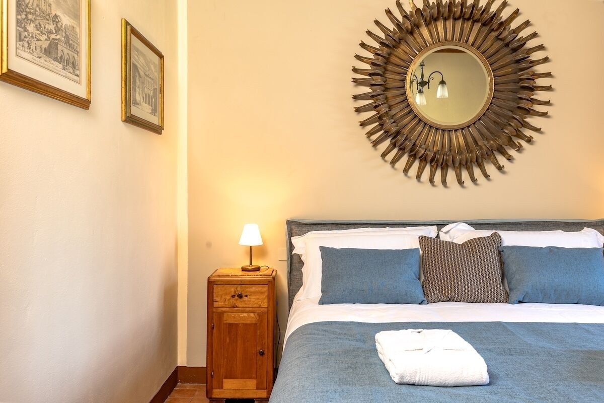 A hotel room with a bed, a nightstand with a lamp, a wall-mounted mirror, and two framed pictures.