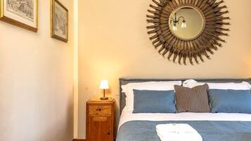 A hotel room with a bed, a nightstand with a lamp, a wall-mounted mirror, and two framed pictures.