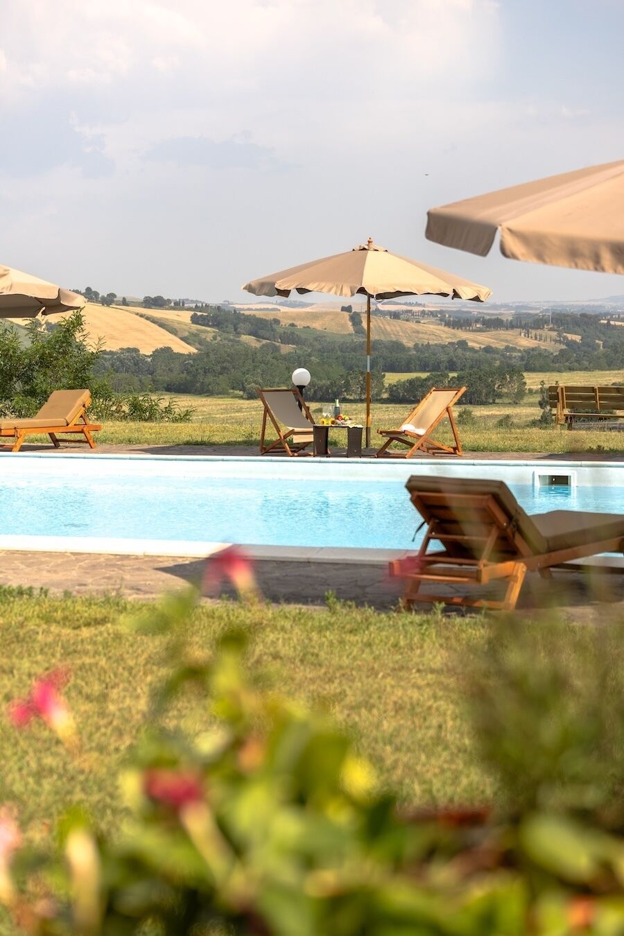 Zona junto a la piscina con sillones reclinables y sombrillas, con vistas a un paisaje pintoresco.